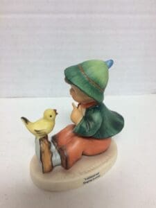 Child figurine with bird on a branch.