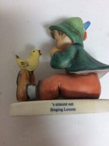 Boy figurine with bird, titled "Singing Lesson".