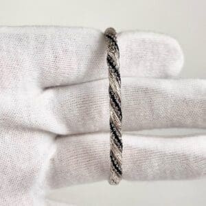 Gloved hand holding a twisted metal bracelet.