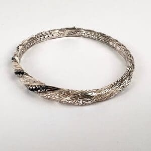 Silver bangle with intricate engraved design.