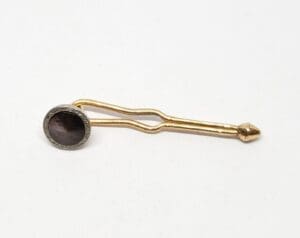 Gold stickpin with dark round gemstone.