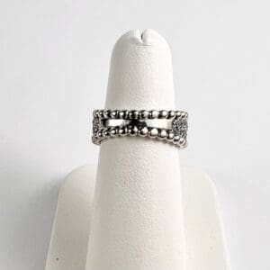 Silver ring with beaded design on stand.