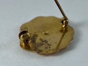 Gold-plated pin with clasp and marking.