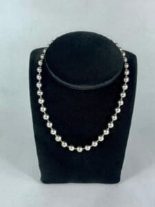Silver beaded necklace on black display stand.