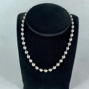 Silver beaded necklace on black display stand.