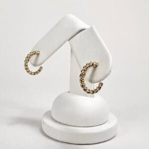Gold twisted hoop earrings on display stand.