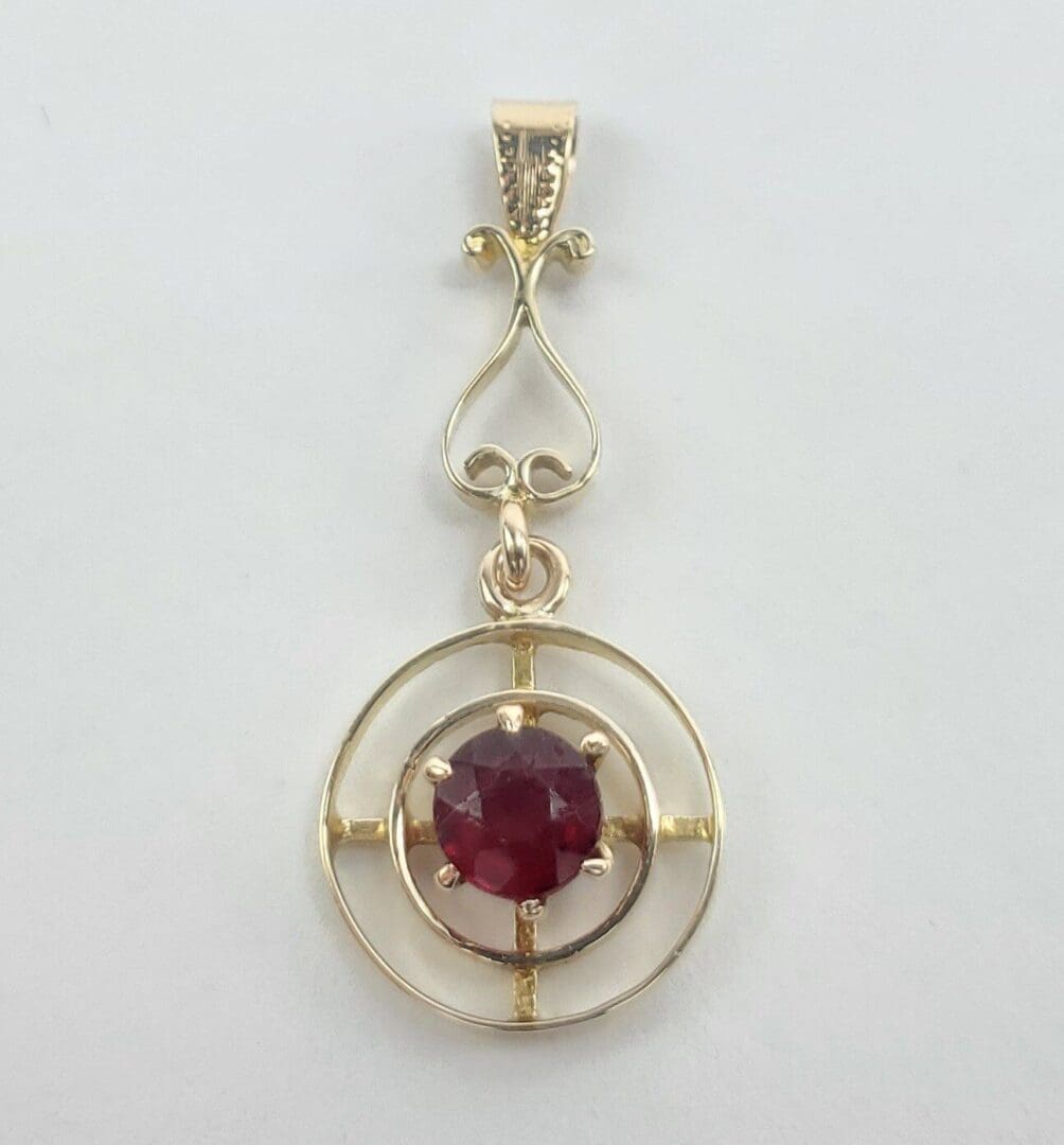 Gold pendant with red gemstone center.