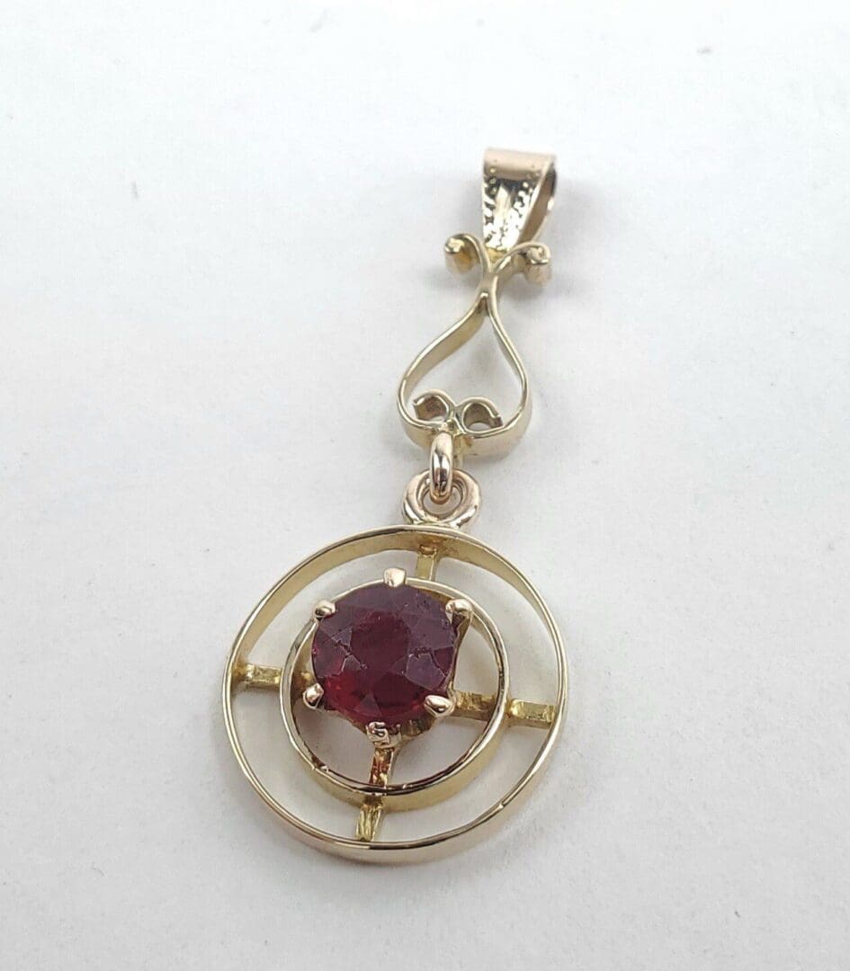 Gold pendant with a red gemstone center.