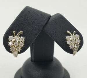 Gold grape cluster earrings on black stand.