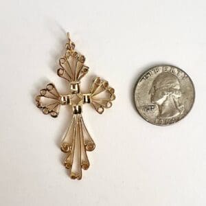 Gold cross pendant next to a quarter.