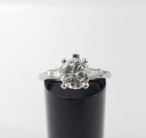 Diamond engagement ring on black display stand.