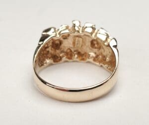 Gold ring with intricate design on top.