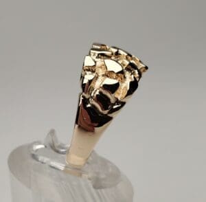 Gold ring with intricate design on stand.