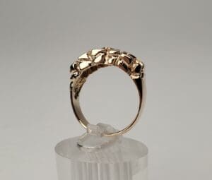 Gold ring with intricate design on stand.