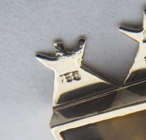 Silver crown-shaped pendant with stamped markings.
