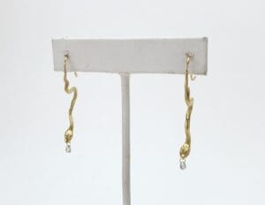 Gold snake-shaped earrings on display stand.