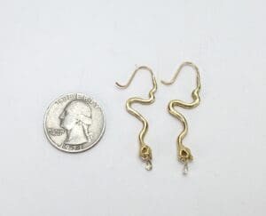 Gold snake earrings beside a quarter.