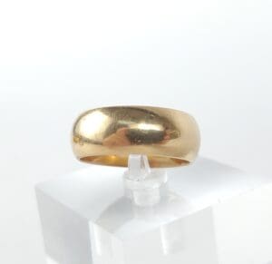 Gold ring displayed on clear stand.