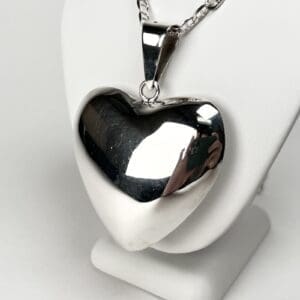 Heart-shaped silver pendant on display stand.