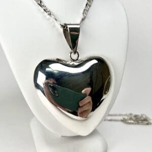 Silver heart-shaped pendant on display stand.