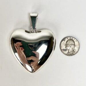 Heart-shaped silver pendant beside a quarter.