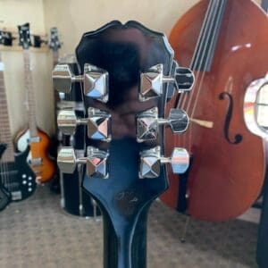 Guitar headstock with tuning pegs, instruments behind.