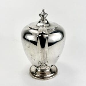 Silver teapot with ornate handle and lid.