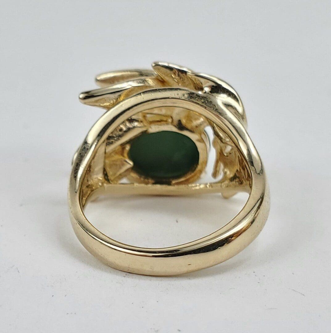 Gold ring with green gemstone, intricate design.