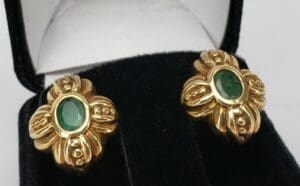 Gold earrings with green gemstones in box.