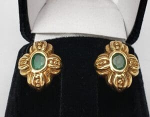 Gold earrings with green gemstones in box.