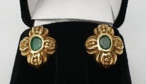 Gold earrings with green gemstones in box.