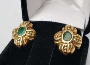 Gold earrings with green gemstones in box.