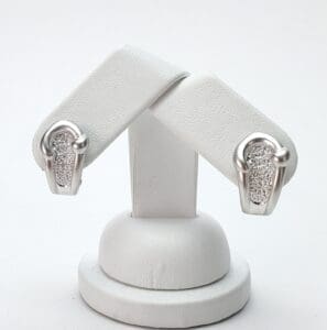 Silver earrings with textured design on stand.