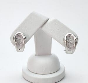 Silver earrings with textured design on stand.
