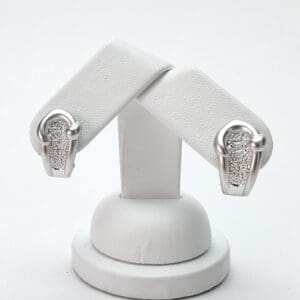 Silver earrings with textured design on stand.