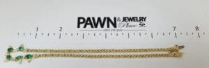 Gold bracelet with green gemstones and ruler.