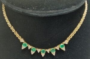 Gold necklace with green gemstones on display.