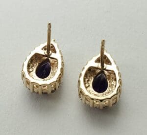 Gold teardrop earrings with dark gemstones.