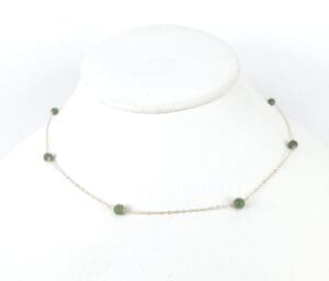 Gold chain necklace with green beads displayed.