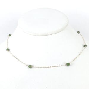 Gold chain necklace with green beads displayed.