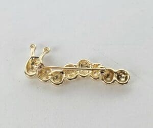 Gold snail-shaped brooch on white background.