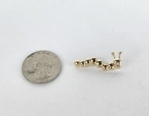 Gold caterpillar charm beside a quarter.