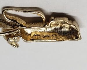 Gold pendant with engraved letters and symbol.