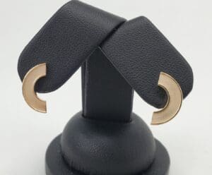 Gold crescent earrings on black display stand.