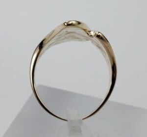 Gold ring displayed on a white stand.