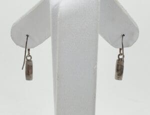 Silver dangle earrings on white stand.