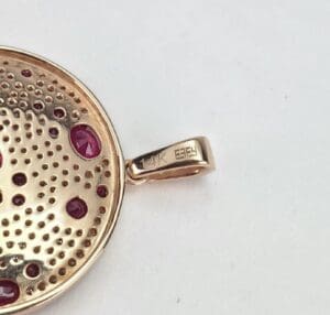 Gold pendant with red gemstones and markings.