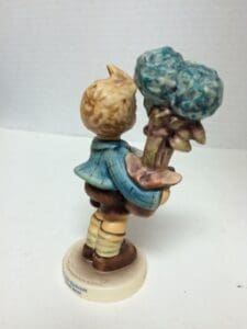 Child figurine holding large bouquet of flowers.