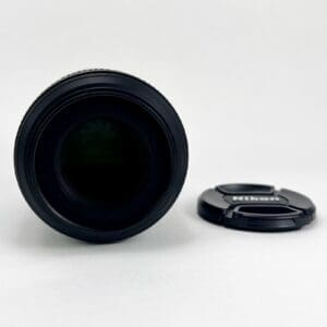 Camera lens with detached Nikon lens cap.