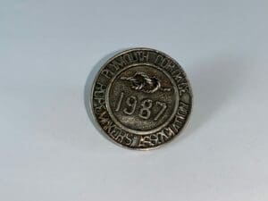 Round metal badge with "1987" engraving.